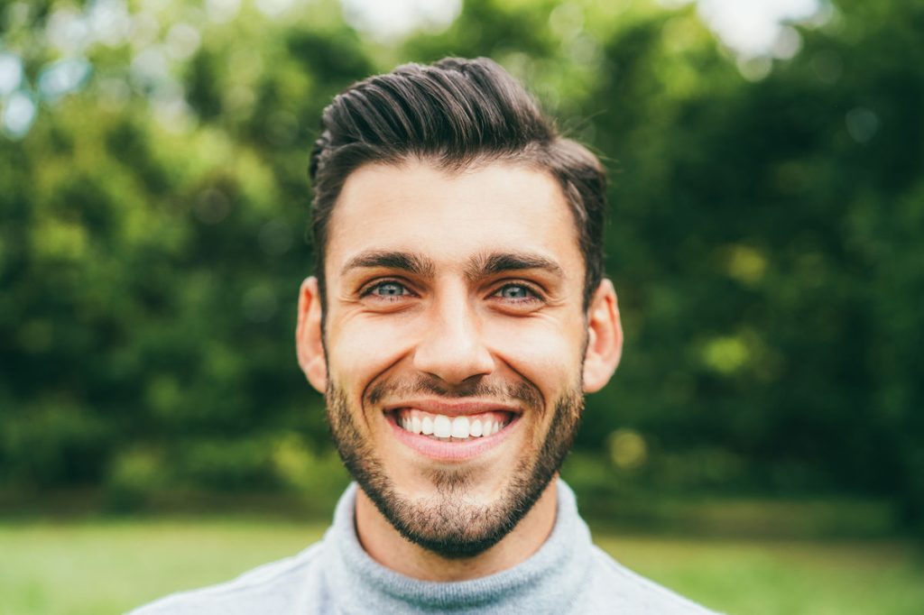 Young happy man looking at camera outdoor - Main focus on nose
