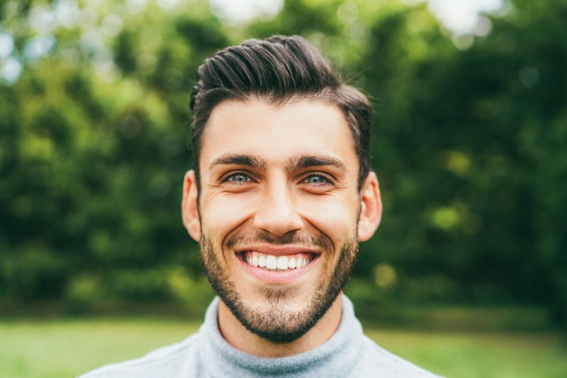 Young happy man looking at camera outdoor - Main focus on nose